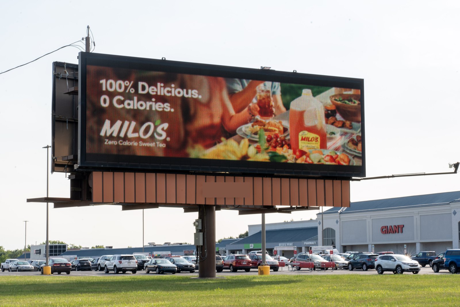A digital billboard advertising a zero-calorie sweet tea brand standing in the parking lot of a Giant grocery store, with the storefront and parked cars behind it.