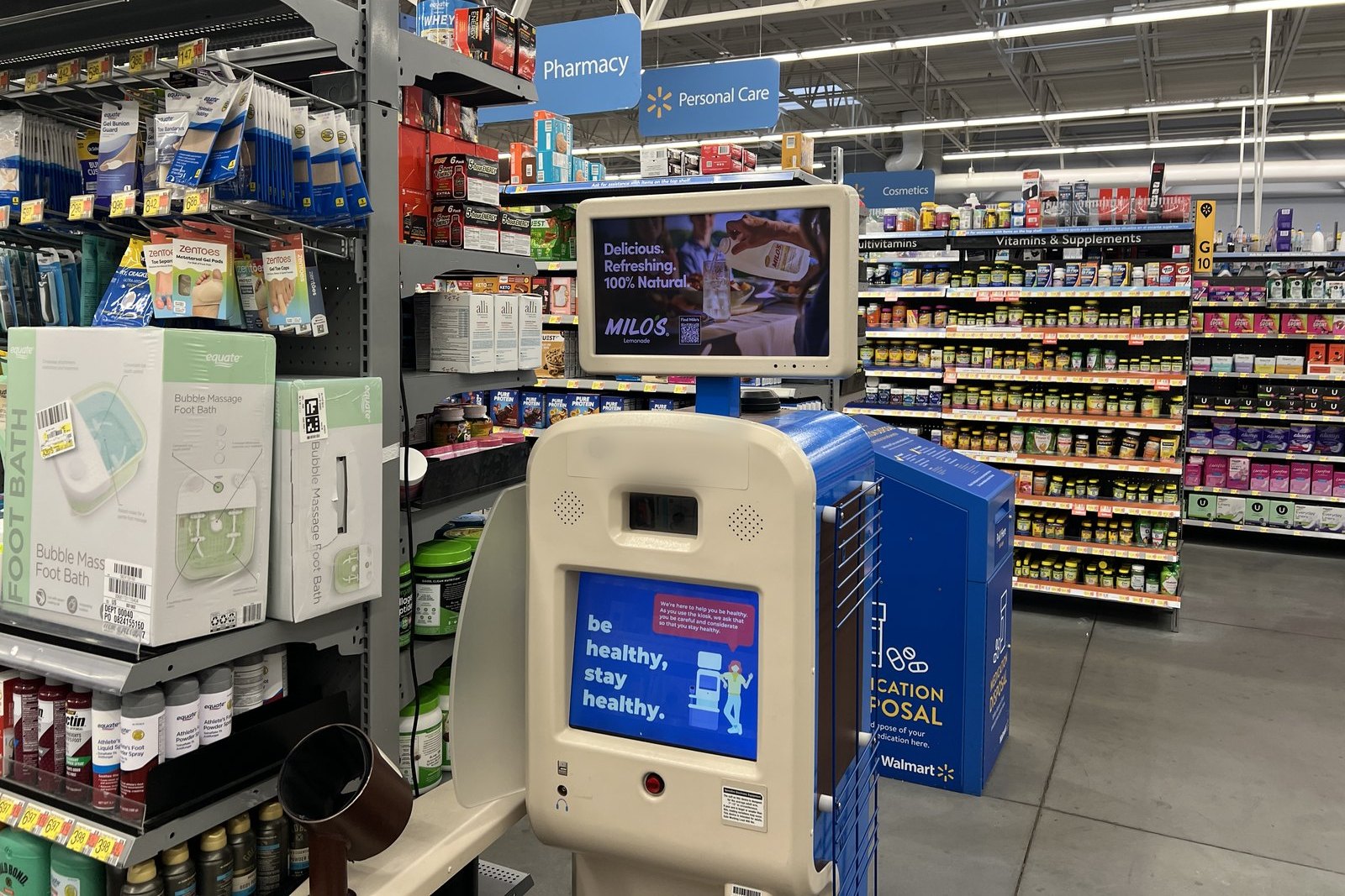 An in-store digital screen inside a mass retailer's pharmacy aisle running an ad for a sweet tea brand, surrounded by product shelving.